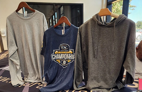 SCAC Volleyball Championship shirts and a hoodie displayed on hangers.
