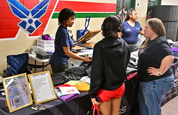 Attendees browse wrestling tournament apparel and merchandise at an event booth.