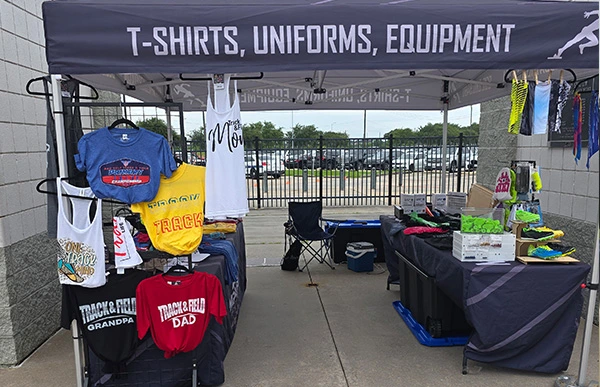 Impress Athletix booth displaying official championship T-shirts and apparel at the 2026 AAU Gulf District Primary Championships.