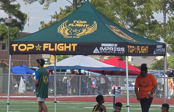 Top Flight Track Club canopy displaying Impress Athletix as a sponsor at an outdoor track meet.