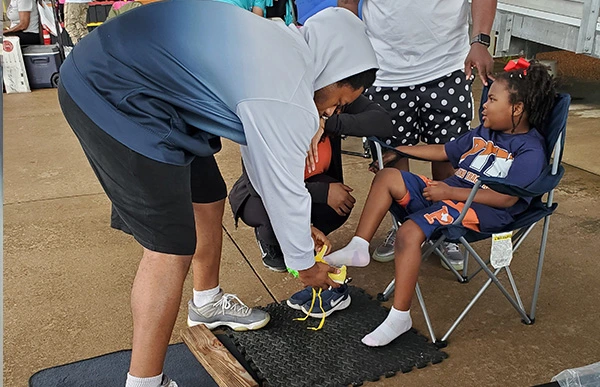 Impress Athletix staff helps a young athlete try on a track spike at Pearland Speed while another child watches.